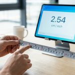 Mains tenant un mètre ruban devant une tablette affichant 2,54 cm/inch pour illustrer la conversion des unités.